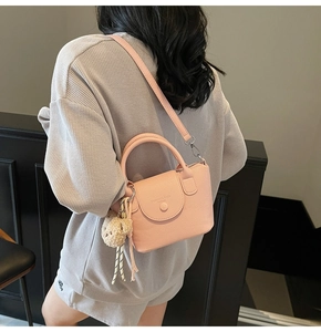 Détail d'un sac à main rose en cuir grainé avec breloque d'ours sur un mannequin femme