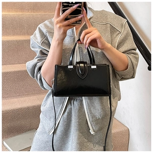 Détail d'un sac à main noir en cuir verni brillant avec boucle argentée en U et deux anses