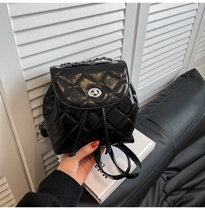 Close-up of black quilted leather backpack with silver rotating lock and metal chain strap