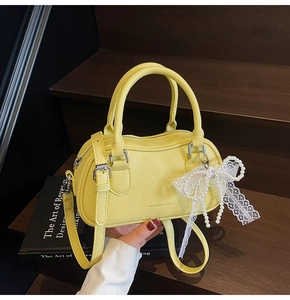 Close-up of yellow pebbled leather Boston bag with pearl lace bow charm on wooden steps
