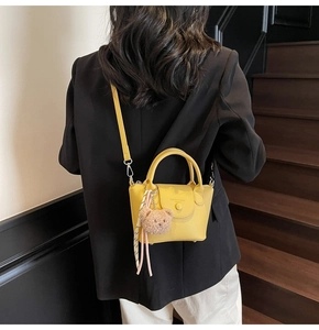 Détail du sac à main jaune texture litchi avec breloque ours et décoration en foulard