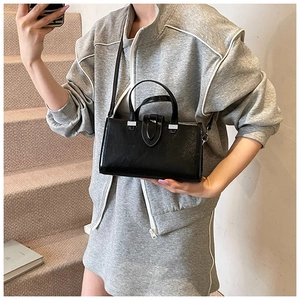 Détail d'un sac à main en cuir ciré noir avec boucle argentée sur fond d'escalier moderne