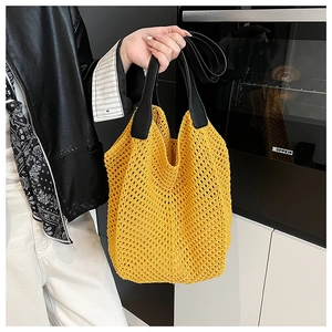 Close-up of a yellow hollow crochet knit tote bag with contrasting black leather handles