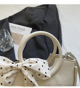 Détail d'un sac à main en cuir grainé crème avec un foulard à pois élégant sur l'anse