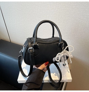 Detail of black pebbled leather Boston bag with pearl lace bow and silver heart charm