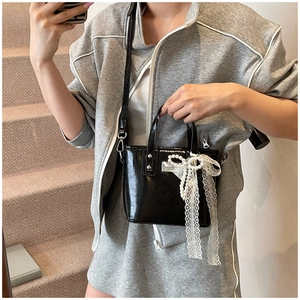 Dettaglio della borsa nera lucida con decorazioni in pizzo bianco e fiocco di perle sul davanti