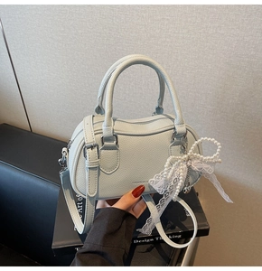 Close-up of mint green litchi leather Boston bag with a pearl lace bow charm