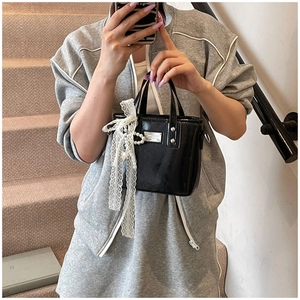 Close-up of black patent leather bucket bag with white lace bow and pearl pendant detail
