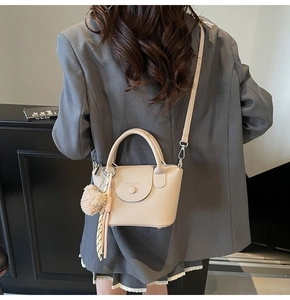 Détail du sac à main beige texturé avec foulard en soie et pompon sur une veste grise