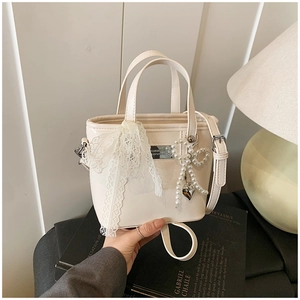 Detail of a beige PU bucket bag featuring lace bow tie and pearl butterfly pendant accents
