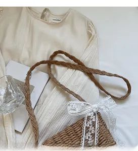 Detail of hand-woven straw crossbody bag with white lace bow and twisted strap