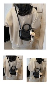 Detail of black patent leather crescent bag featuring a round handle and plush bear charm