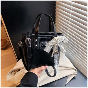 Close-up of black glossy leather bucket bag with pearl lace bow and metal plaque
