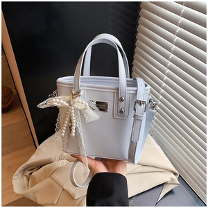 Detail view of a pale blue bucket bag with pearl lace charm and metallic brand plaque