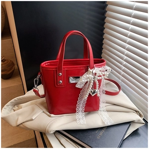 Detail view of red bucket bag featuring white lace bow with pearl and heart charms