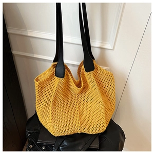 Close-up of yellow hollow crochet tote bag with black leather straps and woven texture