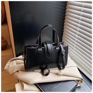Détail d'un sac à main en cuir huilé noir avec boucle argentée sur un trench-coat
