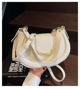 Detail of white lychee leather saddle bag with gold metal hardware on wooden stairs