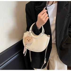 Detail view of cream white crescent bucket bag with wrinkled leather and bear charm accessory
