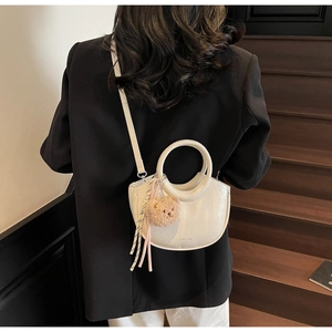 Detail of white crescent bucket bag with leather texture and cute plush bear charm