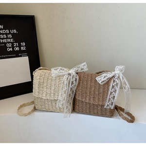 Detail of straw woven crossbody bags in beige and brown with large white lace bows