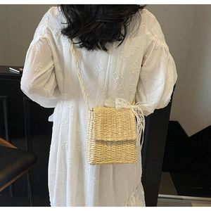 Detail of straw crossbody bag with white lace bow decoration and textured weave