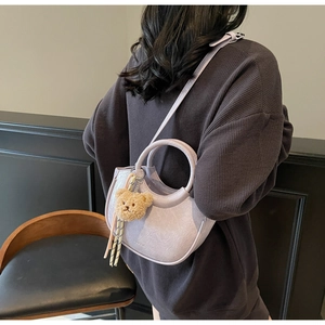 Close-up of a lavender pleated saddle bag featuring a teddy bear charm and silk scarf