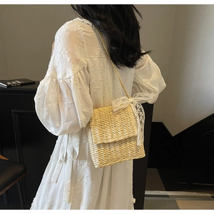 Close-up of a woven straw crossbody bag with delicate white lace bow detailing