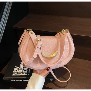 Detail of pink lychee leather saddle bag with gold metal hardware on wooden steps