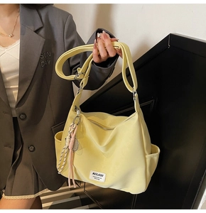 Detail of light yellow canvas tote bag with woven pendant and brand label on side pocket