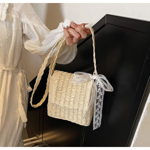 Close-up of beige woven straw crossbody bag featuring delicate white lace bow detail