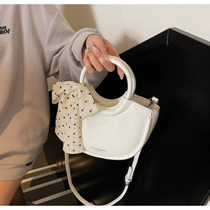 Détail du sac demi-lune blanc en cuir grainé avec un nœud décoratif à pois élégant