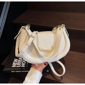Close-up of a white lychee grain saddle bag with gold metal buckle on wooden stairs