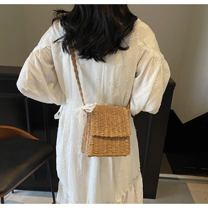 Detail view of woven straw shoulder bag with a large white lace bow and woven strap