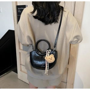 Model wearing a black bucket bag with plush bear charm and silk scarf details