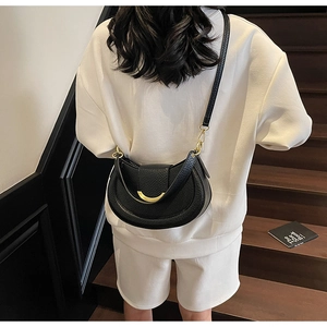 Detail of lychee textured leather saddle bag with gold crescent metal clasp and strap