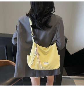 Detail of yellow canvas tote bag featuring adjustable strap and black-white braided charm