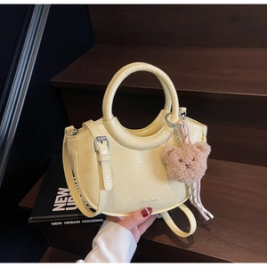 Detail of creamy yellow bucket bag featuring wrinkled leather texture and a plush bear charm