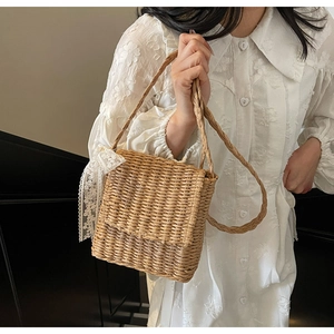 Detail view of woven straw crossbody bag with white lace ribbon and natural texture