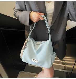 Detail of light blue tote bag with top zipper and woven tassel on a grey suit model