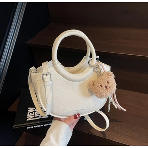 Detail of cream crossbody bucket bag featuring wrinkled leather texture and plush bear charm