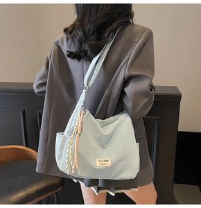Detail of light blue tote bag with contrast tassel charm and white woven brand label