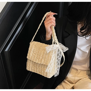 Detail of straw woven crossbody bag featuring a delicate white lace bow and woven strap