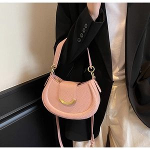 Close-up of a pink litchi leather saddle bag with a crescent gold buckle on a suit