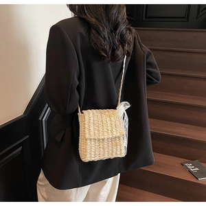 Detail of hand-woven straw crossbody bag with white lace bow on elegant model