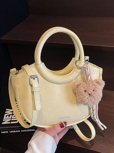 Pale yellow patent leather bucket bag with top handle and brown plush bear charm