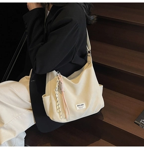 Detail of off-white tote bag with woven pendant on model standing on wooden stairs