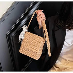 Detailed side view of straw crossbody bag with white lace bow and woven shoulder strap