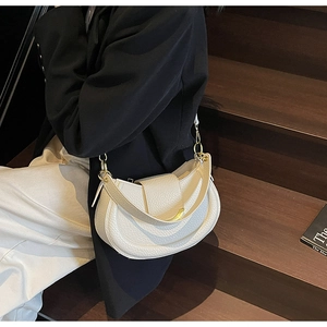 Close-up of cream pebble leather saddle bag with gold hardware on wooden stairs