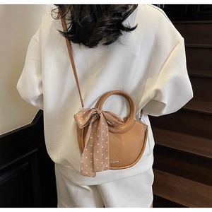 Détail du sac lune en cuir marron avec foulard à pois sur l'anse et fini texturé
